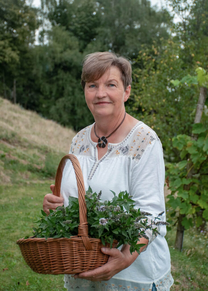 Ein Portrait von Melitta. Sie hält einen Korb mit vielen Kräutern in den Händen.